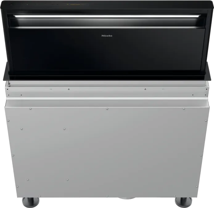 Zostupná ventilačná jednotka Miele s čiernou sklenenou čelnou stenou, čiastočne vysunutou z puzdra z ušľachtilej ocele.